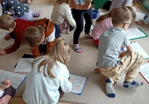 Dzieci kolorują obrazki siedząc na dywanie