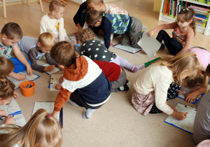 Dzieci kolorują obrazki siedząc na dywanie