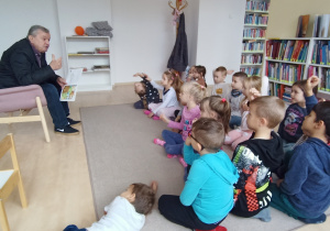 Dzieci siedzą na dywanie w sali biblioteki i słuchają pana Włodzimierza