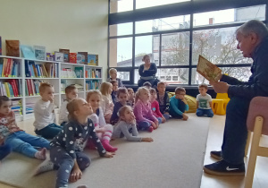Dzieci siedzą na dywanie w sali biblioteki i słuchają pana Włodzimierza