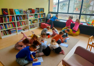 Dzieci w bibliotece kolorują ilustracje.