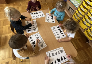 Dzieci przy stolikach wykonują kartę pracy - łączenie ilustracji.