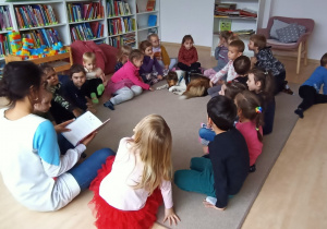 Dzieci siedzą na dywanie i słuchają czytanego opowiadania.