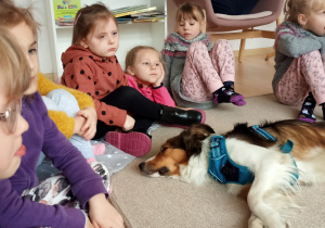 Dzieci siedzą na dywanie i słuchają czytanego opowiadania.
