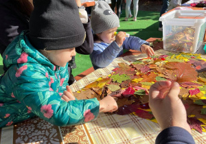 Dzieci z rodzicami przyklejają liście do pracy plastycznej.