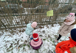 Dzieci obserwują domki dla małych zwierząt/gryzoni pośród gałęzi i śniegu.