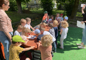 Dzieci wykonują zadania przy stole w ogrodzie przedszkolnym.