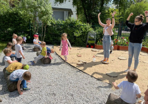 Dzieci wraz z nauczycielkami ćwiczą w ogrodzie przedszkolnym.