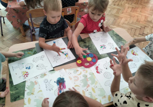 dzieci siedzą przy stoliku i malują palcami