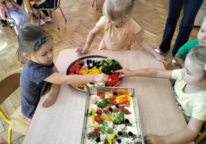 dzieci układają warzywa na cieście