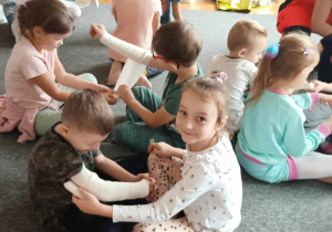 Dzieci w parach ćwiczą zakładanie bandaża.