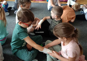 Dzieci w parach ćwiczą zakładanie bandaża.
