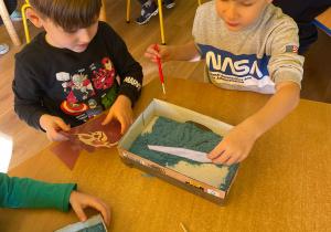 Dzieci wykopują puzzle ze szkieletem dinozaura.