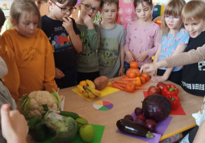 Dzieci pozują przy straganie z owocami i warzywami