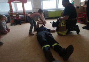 Dziecko próbuje ułożyć strażaka w pozycji bezpiecznej.