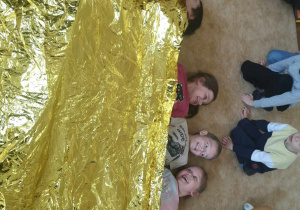 Dzieci leżą pod kocem termicznym.
